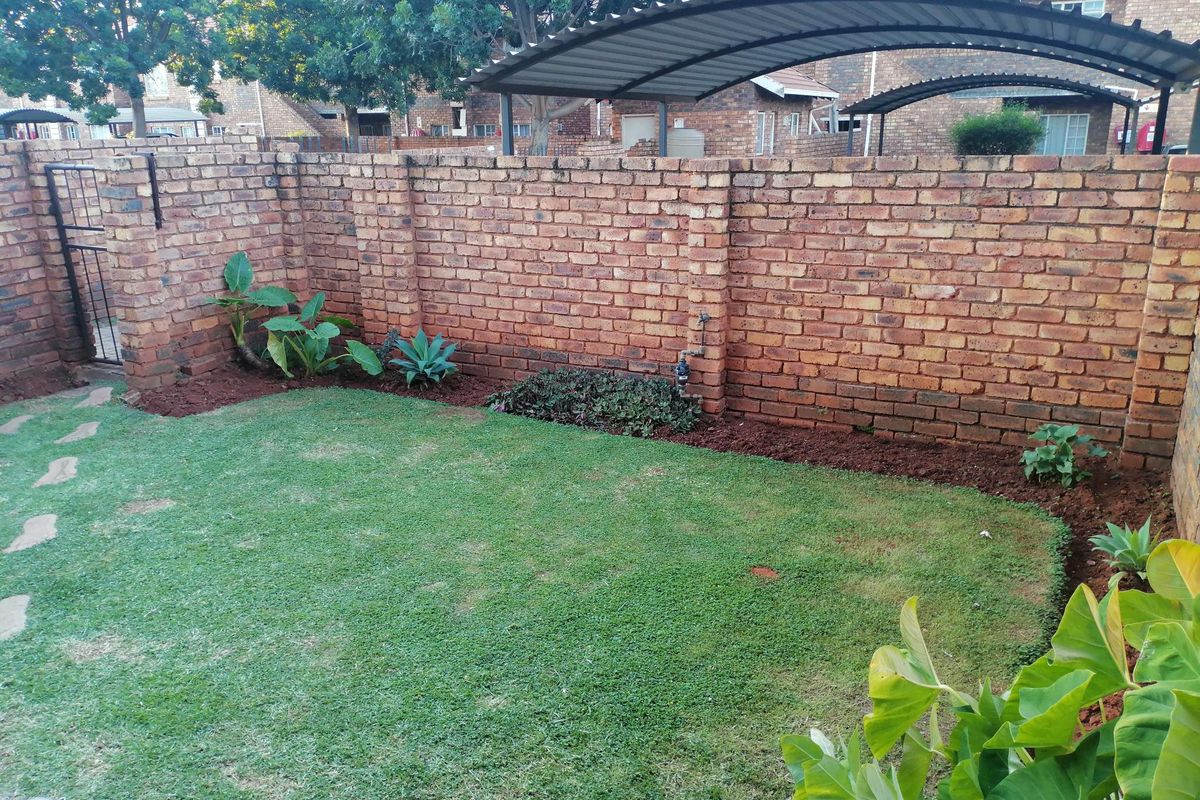 A private rear garden featuring a manicured lawn, established garden beds, and a secure perimeter brick wall with a metal gate.