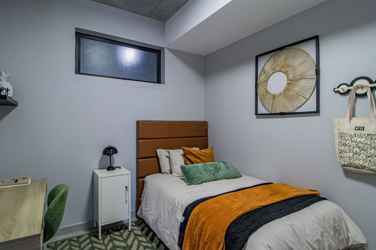 A compact bedroom featuring a high-set horizontal window, neutral wall finishes, and an exposed concrete ceiling detail.