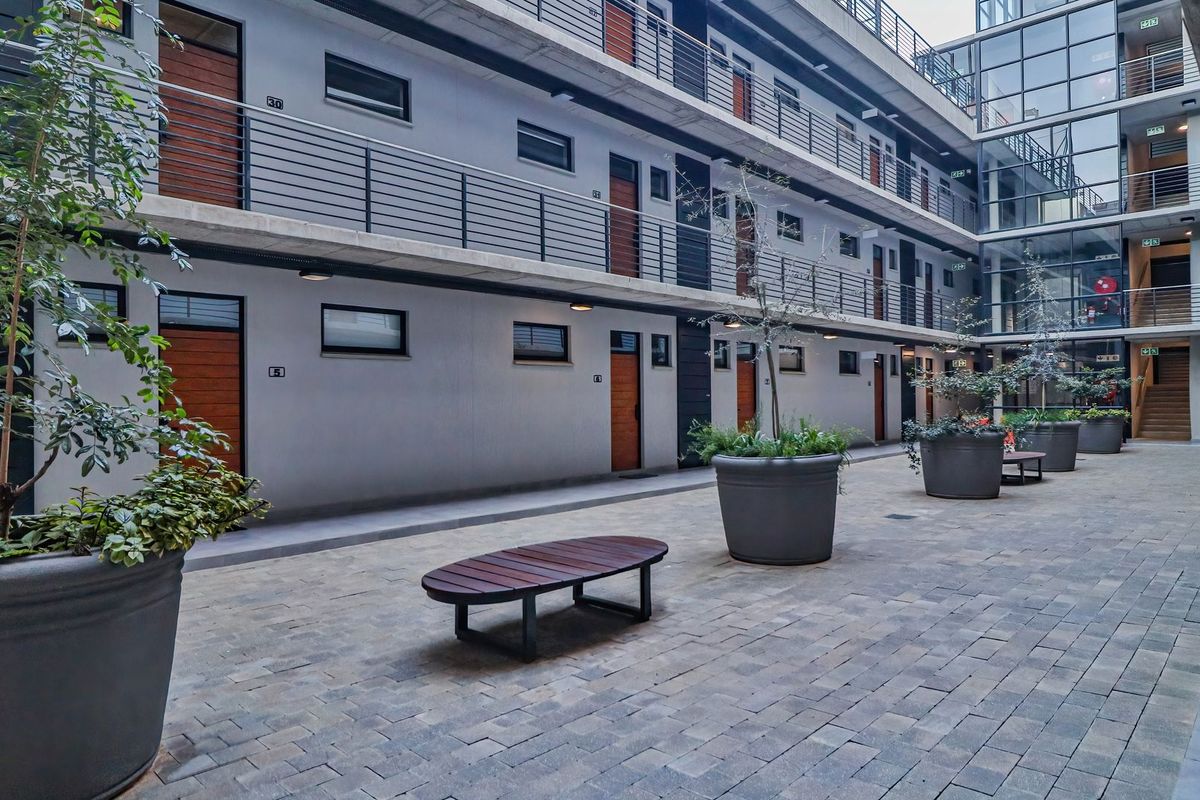 A modern apartment complex courtyard featuring paved flooring, multi-level walkways with metal railings, and access to multiple residential units.