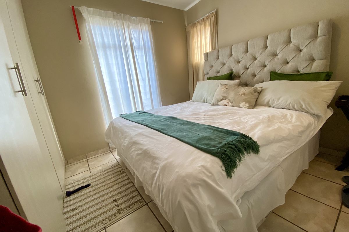 A cozy bedroom featuring built-in wardrobes, tiled flooring, and large windows that allow for natural light.