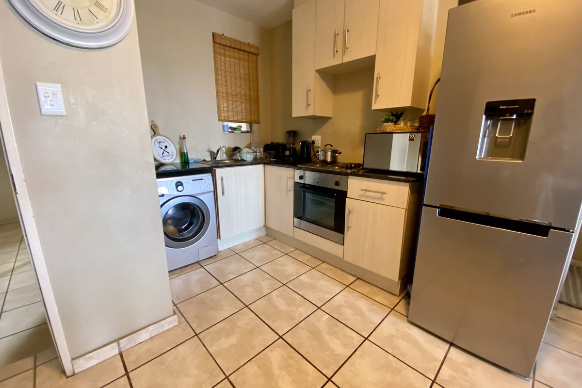Compact kitchen featuring light wood-finish cabinetry, integrated oven and hob, and dedicated space for a washing machine with tiled flooring.