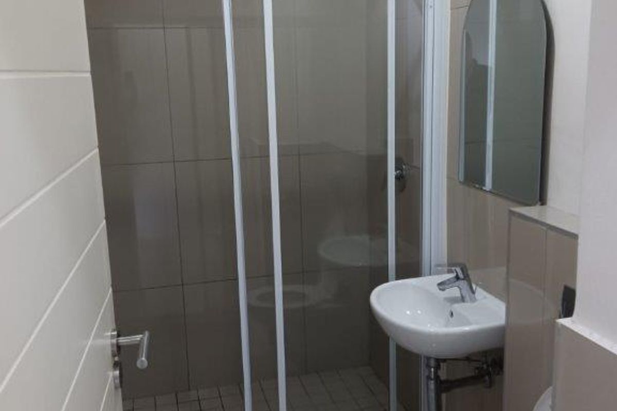 A compact, modern bathroom featuring a glass-enclosed shower, wall-mounted basin, and toilet with neutral floor-to-ceiling tiling.