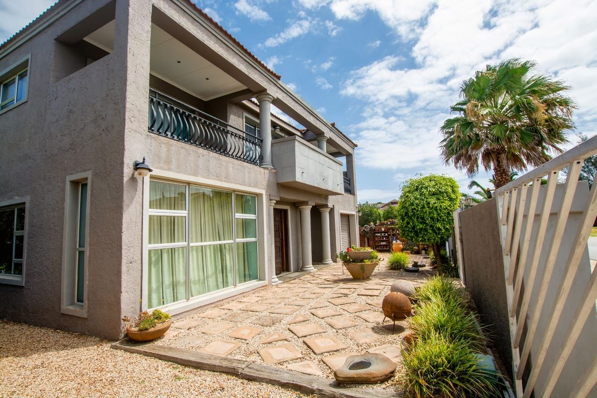 A view of the rear exterior of the house, featuring a paved patio area, covered balcony, and landscaped garden space.