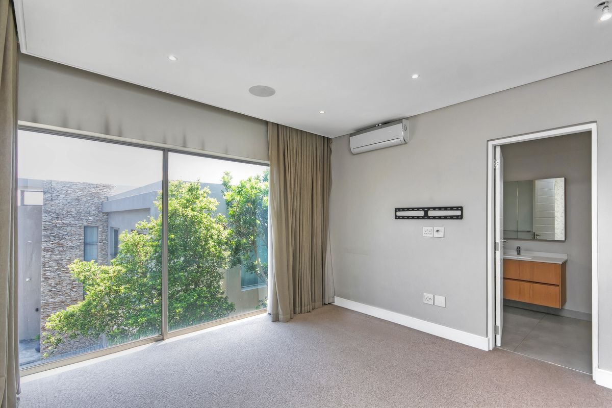 A spacious bedroom featuring neutral carpeting, large sliding glass doors, a wall-mounted air conditioning unit, and an en-suite bathroom.