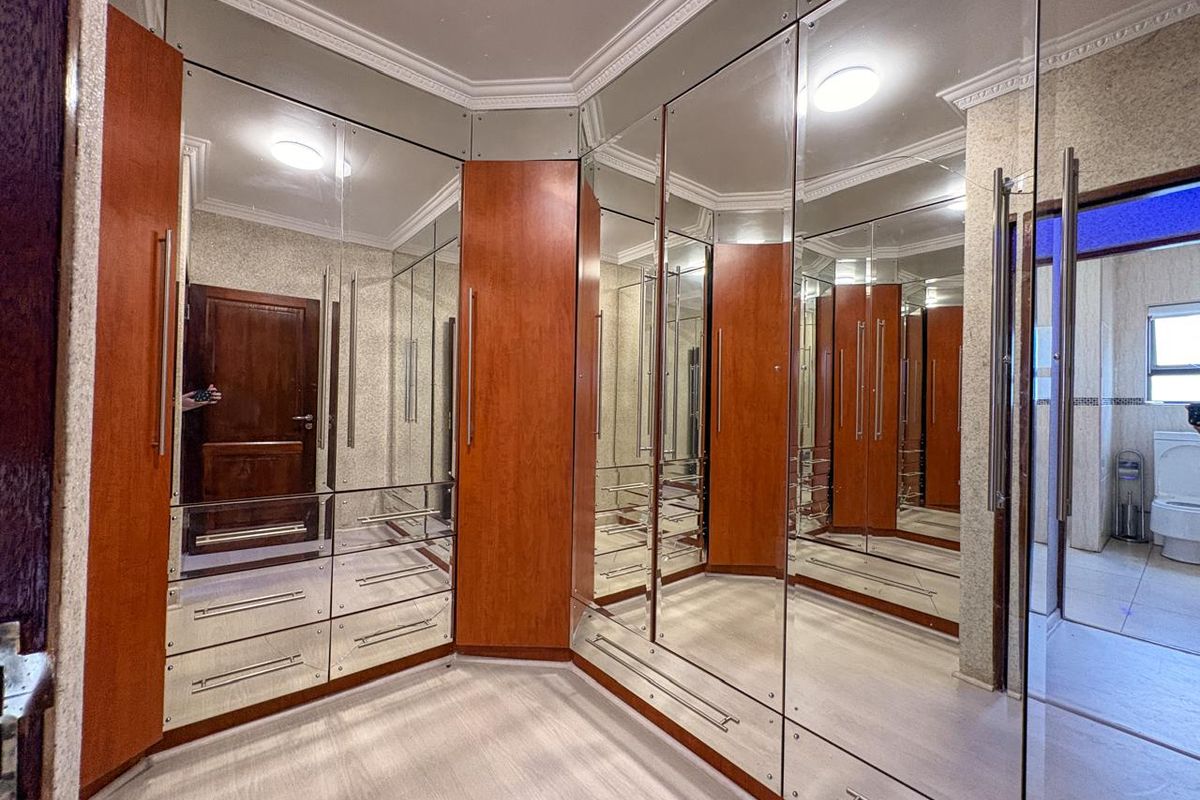 A walk-in dressing room featuring extensive floor-to-ceiling mirrored cabinetry with wood-tone accents and crown molding detail.