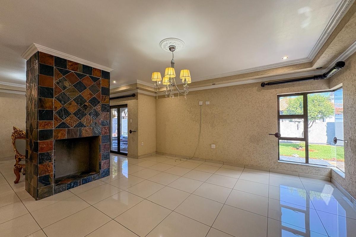 Spacious living area featuring large polished floor tiles, a prominent slate-tiled fireplace, and decorative ceiling cornicing with a central chandelier.