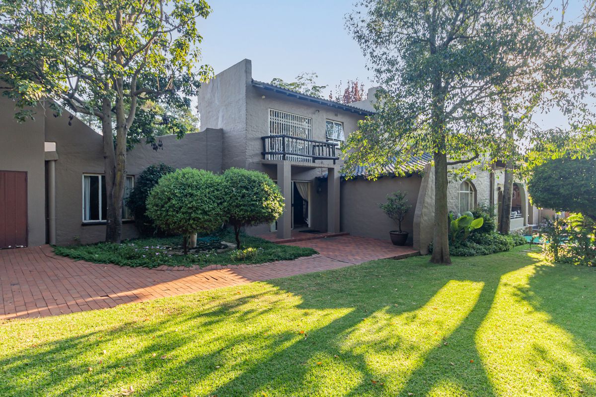 Rear view of the house featuring a paved patio area, established garden, and a balcony overlooking the backyard.