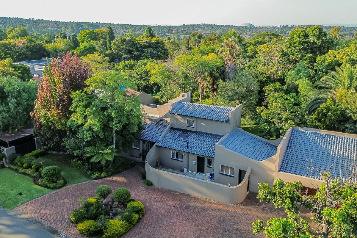 Aerial view of a residential property featuring a multi-level house with a tiled roof, paved driveway, and lush surrounding garden.