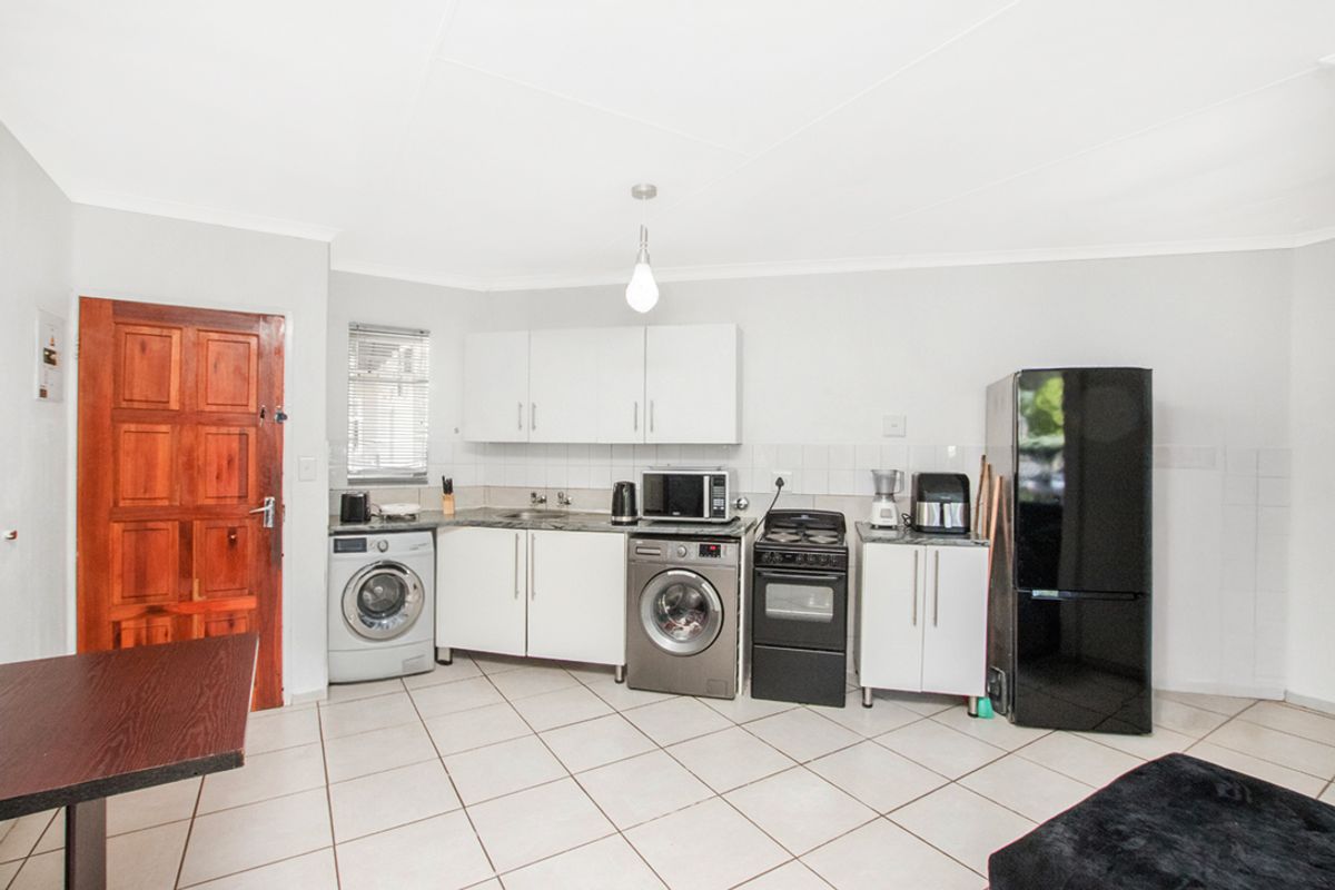 Functional kitchen area featuring white cabinetry, tiled flooring, and integrated space for laundry appliances and a freestanding stove.