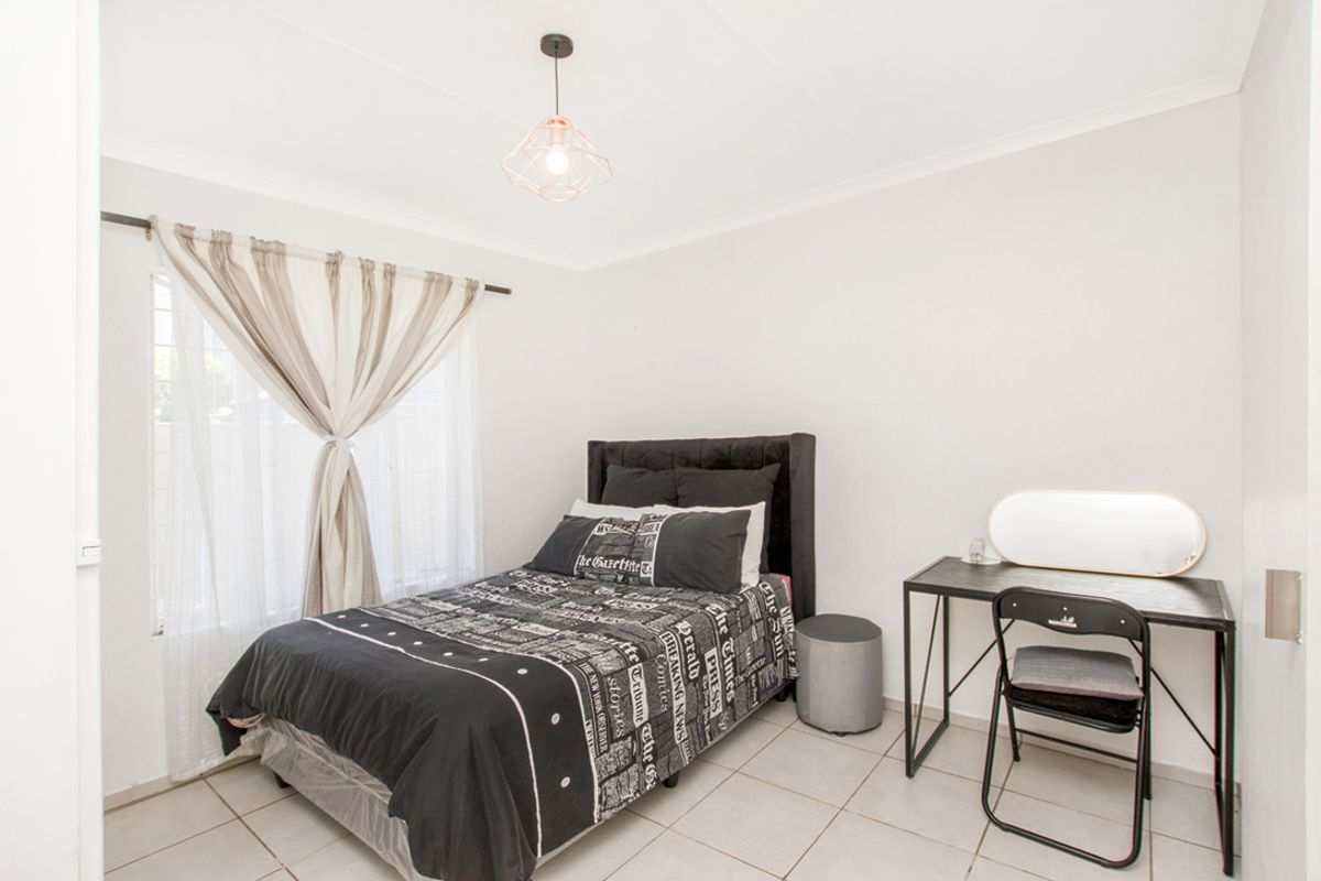 A bright bedroom featuring neutral tiled flooring, white walls, and a modern pendant light fixture.