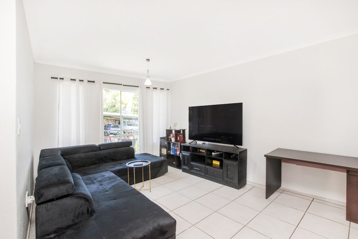 A bright living room featuring neutral floor tiles, a sliding glass door providing natural light, and a clean, minimalist layout.