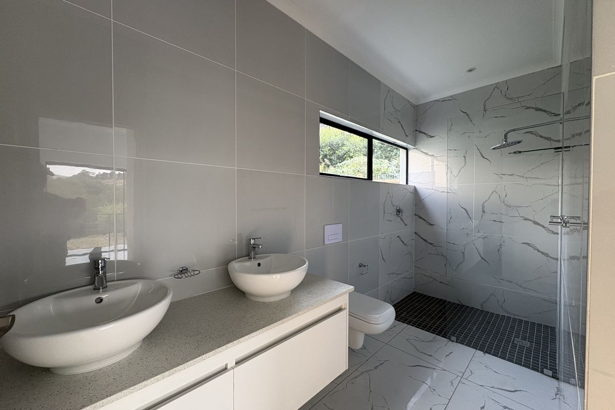 Modern bathroom featuring a double vanity with stone countertop, wall-mounted toilet, and a spacious walk-in shower with marble-look wall tiles.