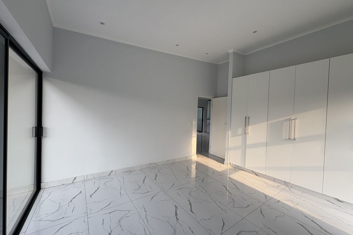 A bright, modern bedroom featuring large-format marble-look floor tiles, recessed ceiling lighting, and extensive built-in white cabinetry with sleek handles.