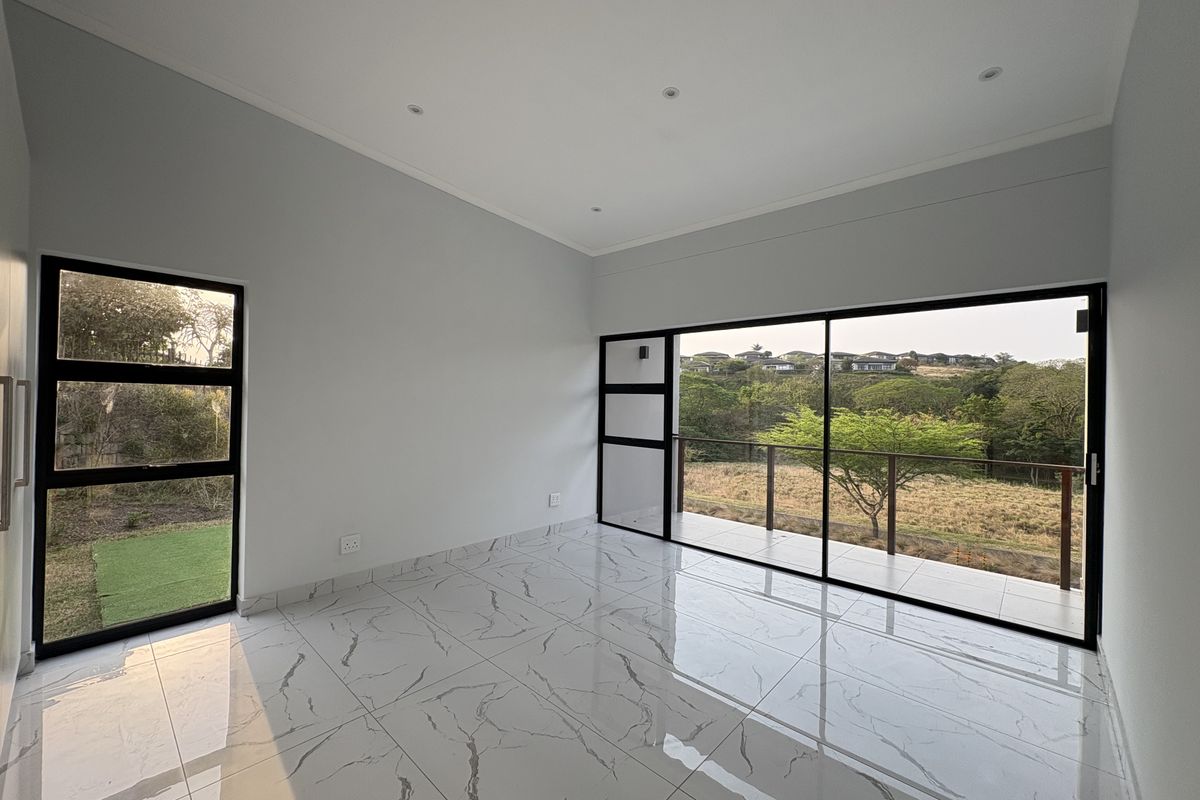 A bright, modern living room featuring large black-framed sliding glass doors that open onto a balcony with scenic landscape views and polished marble-look floor tiles.