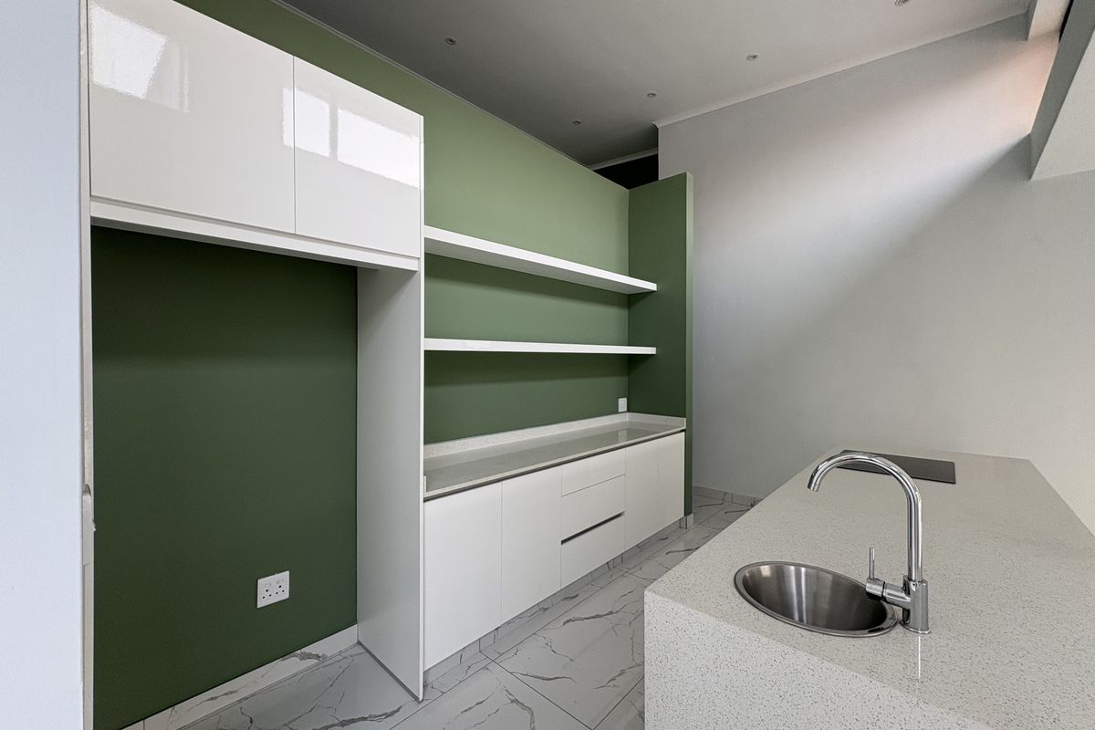 Modern kitchen featuring white cabinetry, stone countertops, a central island with a stainless steel sink, and green accent walls with open shelving.