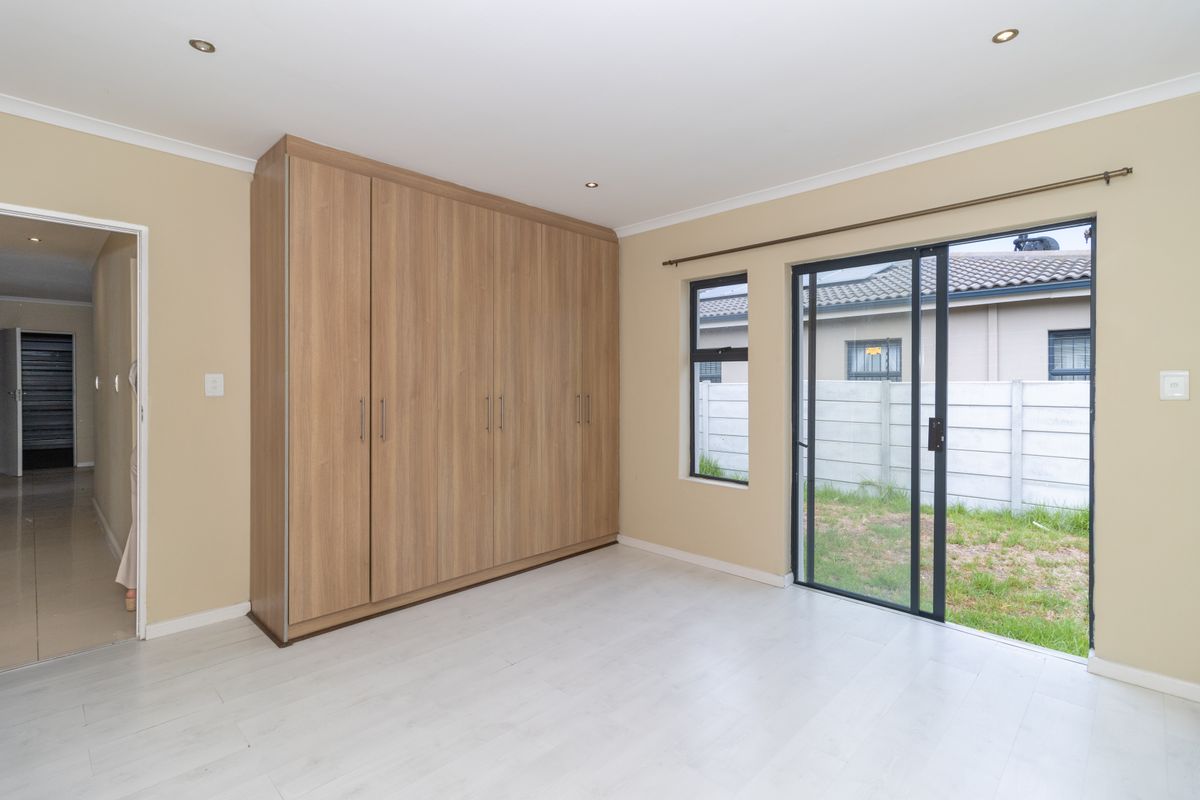 A bright bedroom featuring built-in wooden cabinetry, light-toned flooring, and sliding glass doors providing direct access to the rear garden.