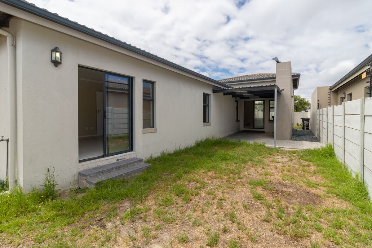 Rear view of the property featuring a paved patio area, covered outdoor space with a chimney, and a private garden enclosed by boundary walls.
