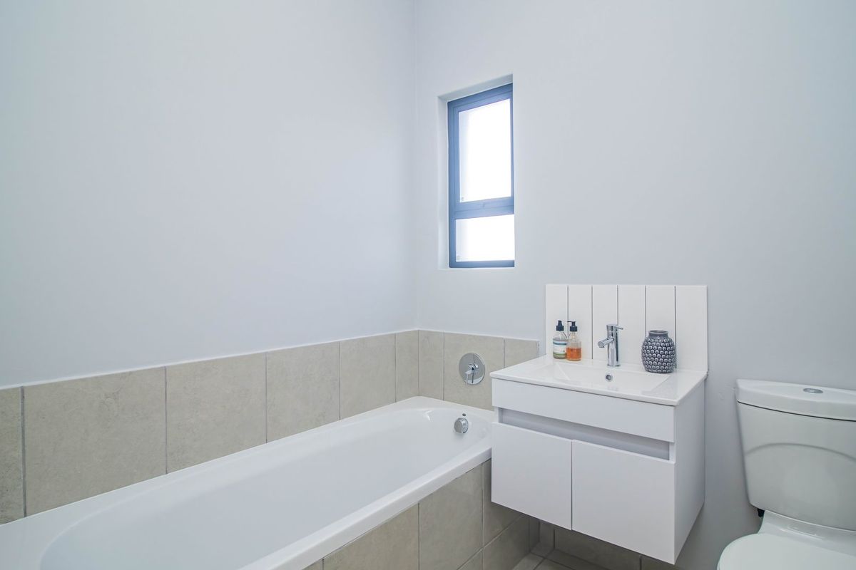 A clean, modern bathroom featuring a white vanity with integrated basin, a bathtub with tiled surround, and a standard toilet.