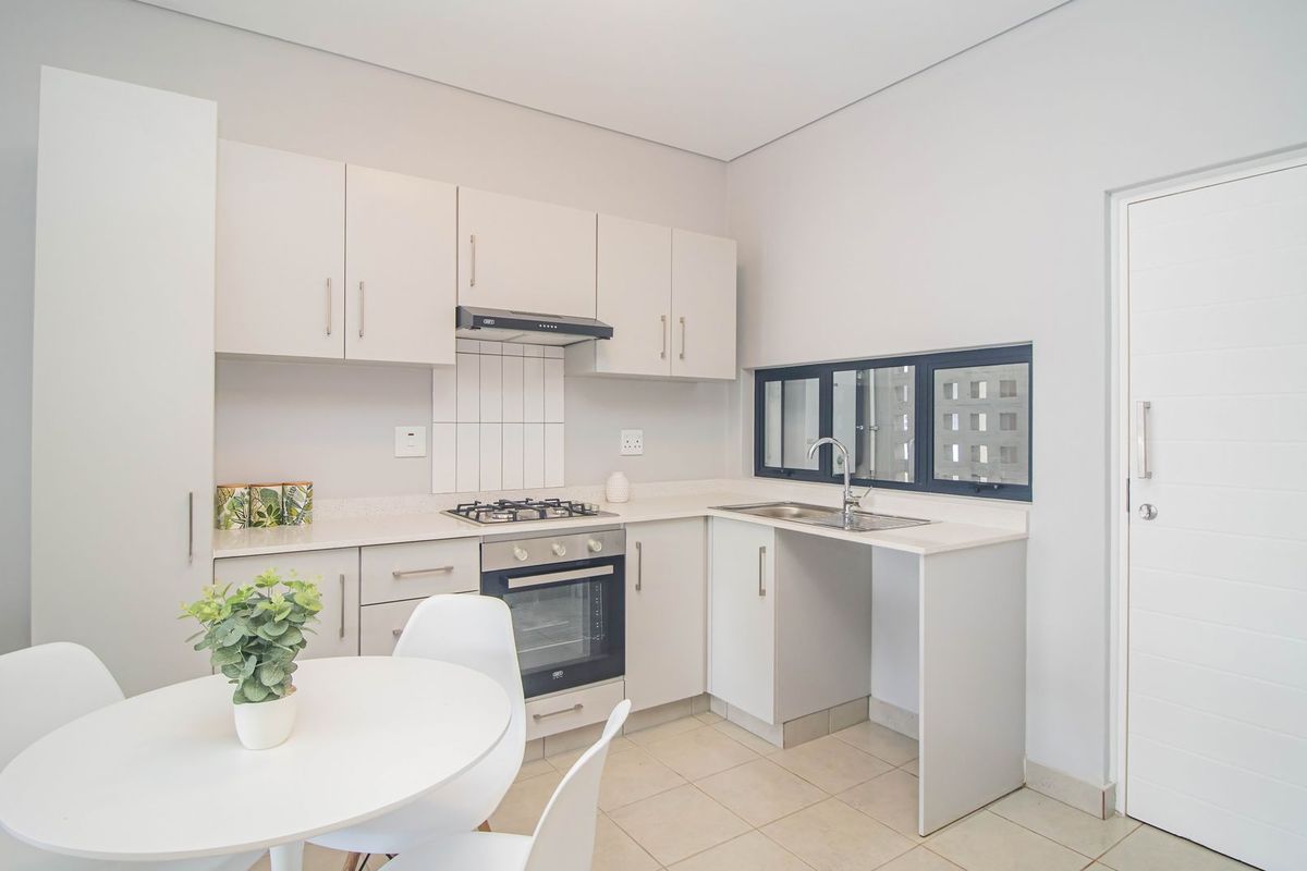 Modern kitchen featuring white cabinetry, built-in gas hob, oven, extractor fan, and stainless steel sink, with tiled flooring and neutral finishes.