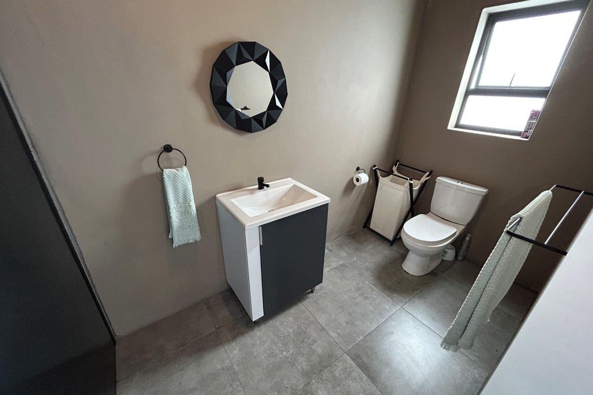 A modern bathroom featuring a vanity cabinet with a basin, a toilet, and tiled flooring, finished with neutral wall tones and a window for natural light.
