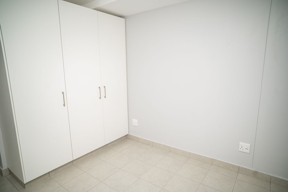 A clean, empty bedroom featuring neutral tiled flooring and built-in white cabinetry with modern handles.