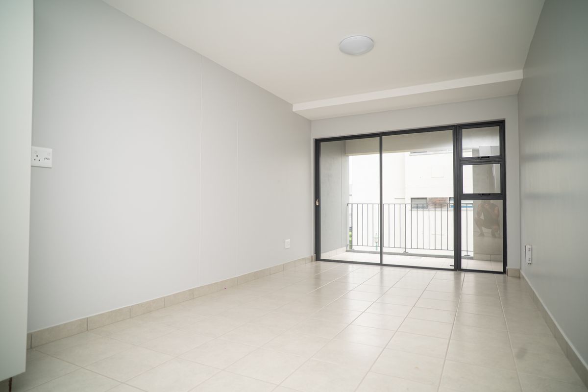A bright, empty living area featuring neutral tiled flooring and large sliding glass doors that open onto a private balcony.