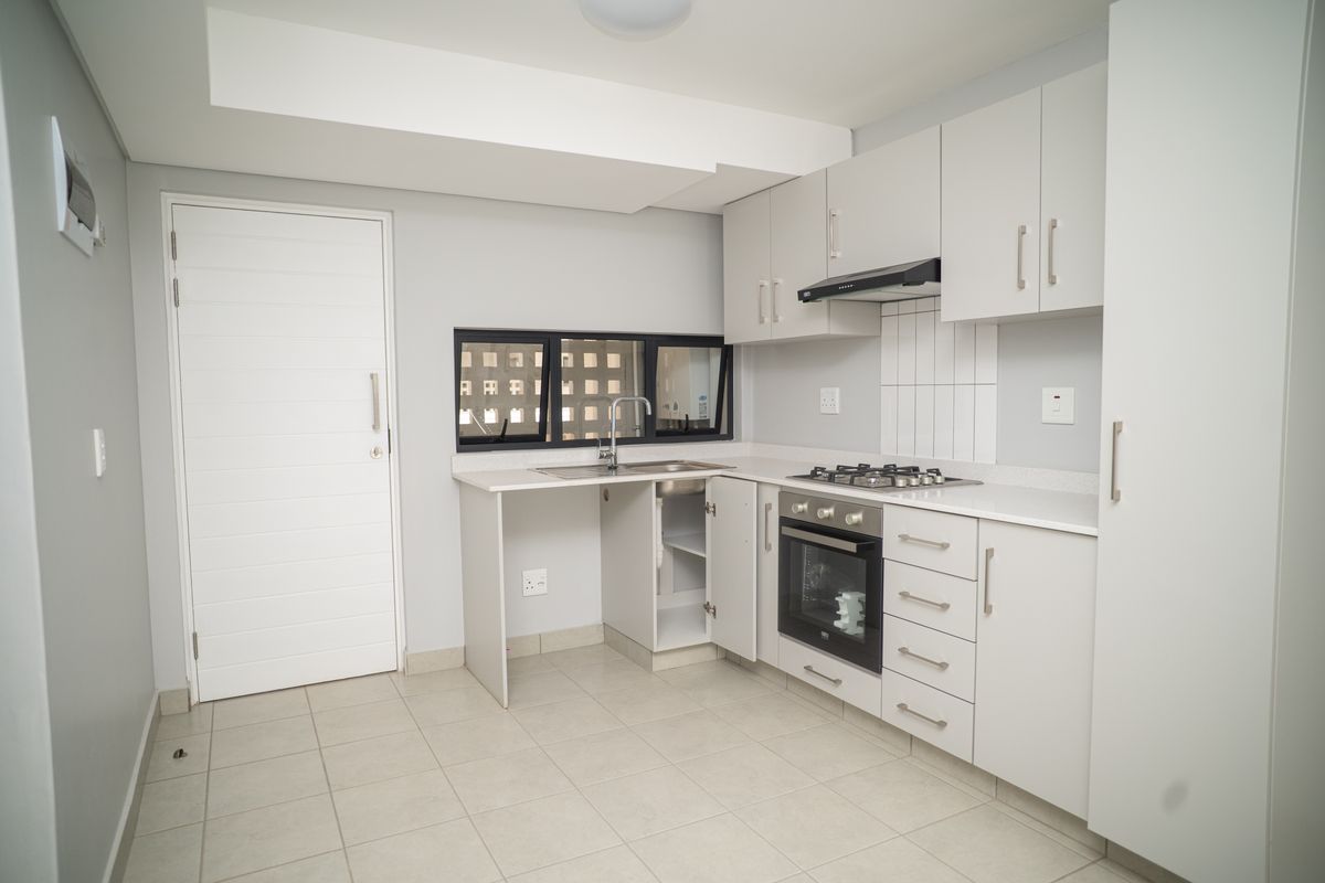 Modern kitchen featuring light grey cabinetry, built-in gas hob, oven, extractor fan, and tiled flooring with a functional layout.