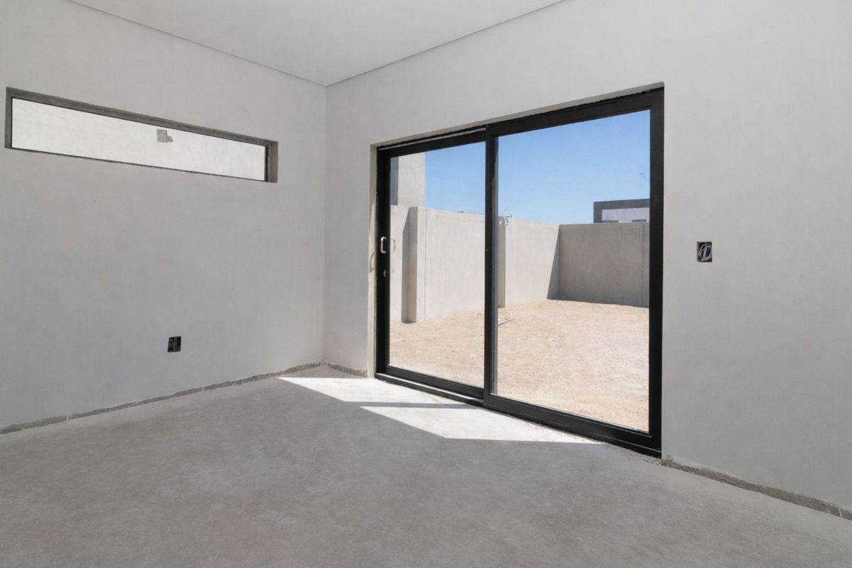 An empty, unfinished bedroom featuring smooth plastered walls, a horizontal clerestory window, and black-framed sliding glass doors leading to an outdoor area.