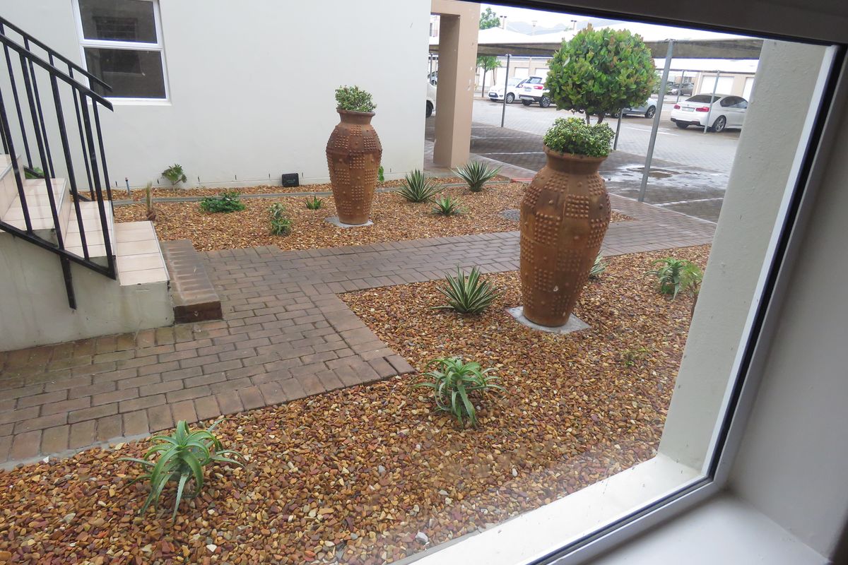 A view from a window overlooking a landscaped rear courtyard featuring a paved walkway, gravel garden beds, and a metal staircase.