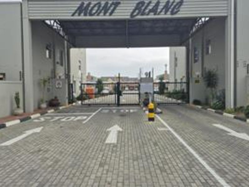 The main entrance to the Mont Blanc apartment complex, featuring a secure gated access point with paved driveway and perimeter electric fencing.