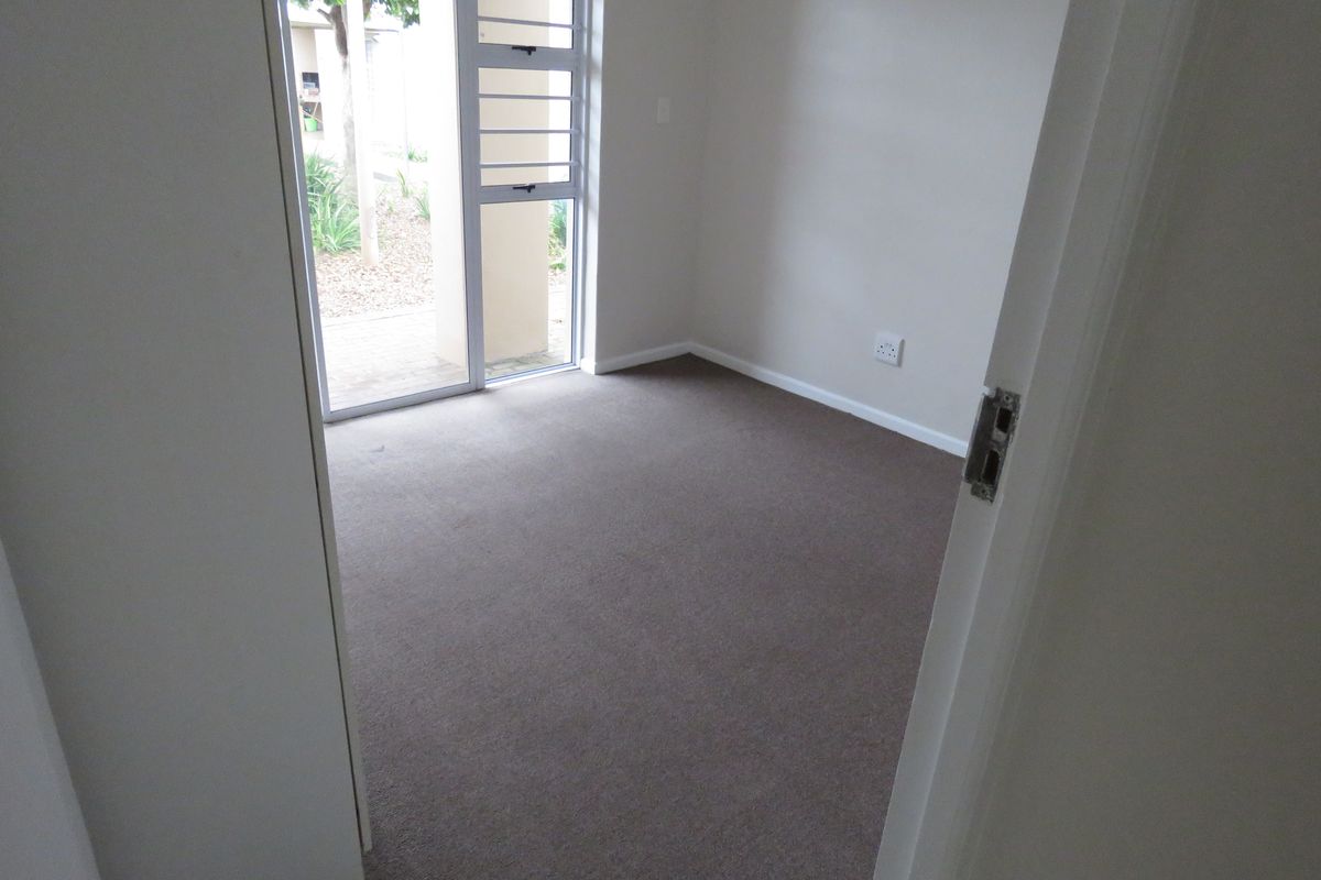 A clean, empty bedroom featuring neutral carpeting and a large aluminium sliding door providing natural light and access to the exterior.