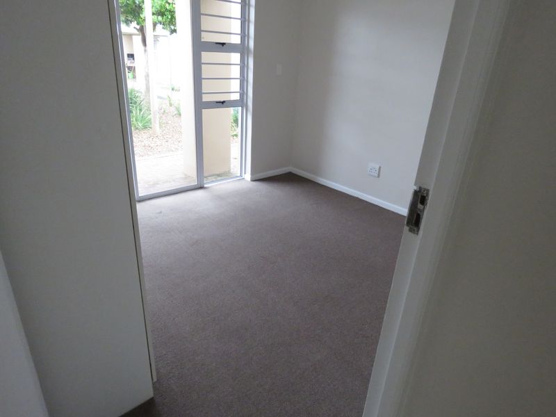 A clean, empty bedroom featuring neutral carpeting and a large aluminium sliding door providing natural light and access to the exterior.