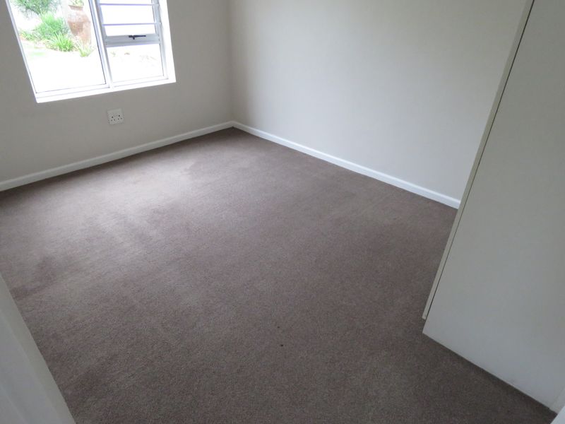 A clean, empty bedroom featuring neutral wall tones, carpeted flooring, and a built-in cupboard, offering a blank canvas for personalization.