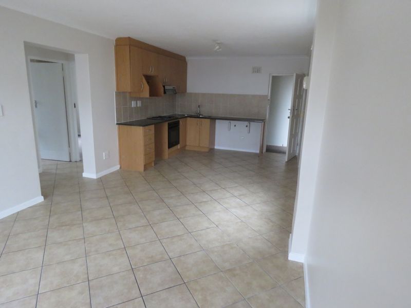 An open-plan kitchen area featuring light wood cabinetry, laminate countertops, built-in oven, hob, and tiled flooring throughout the living space.