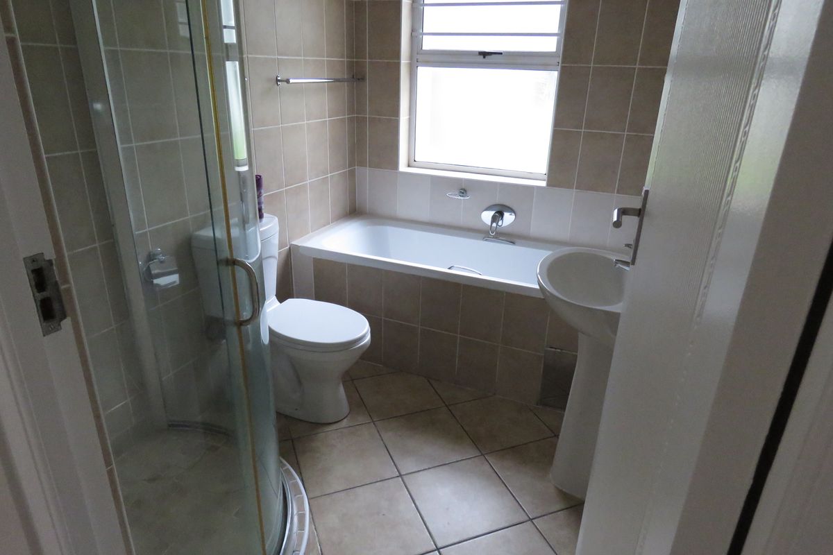 A functional bathroom featuring a shower enclosure, bathtub, pedestal sink, and toilet with neutral wall and floor tiling.