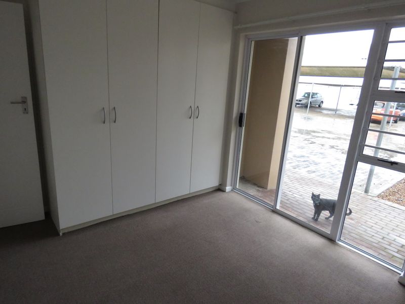 A bright, empty bedroom featuring built-in cupboards and a sliding glass door providing access to the exterior area.