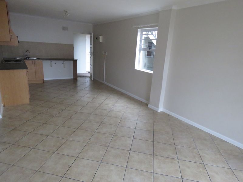 An open-plan living and kitchen area featuring neutral tiled flooring, built-in cabinetry, and a louvered window, offering a clean and versatile living space.