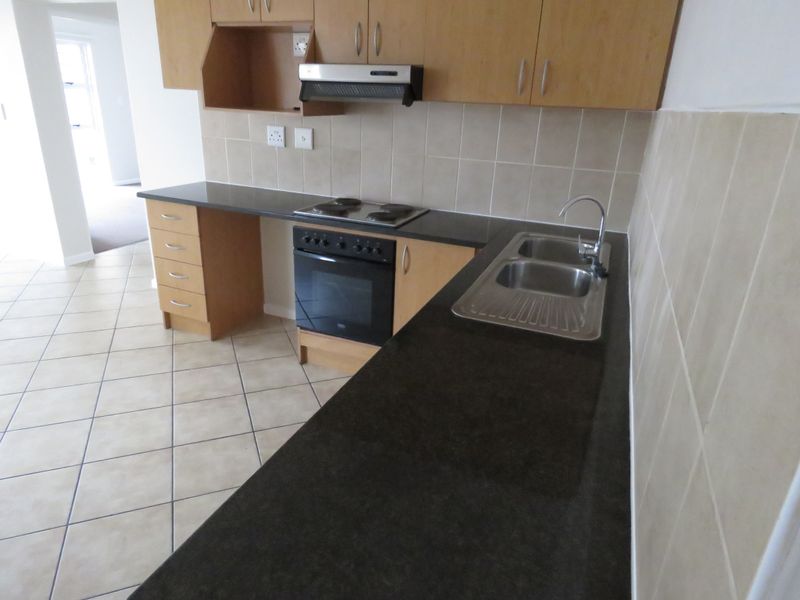 A functional kitchen featuring light wood cabinetry, dark countertops, a built-in oven with hob, and tiled flooring, presented in a clean, empty state.