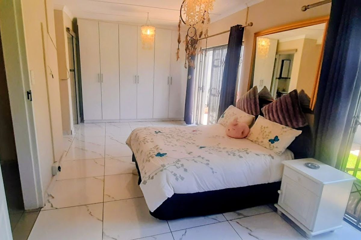 Spacious bedroom featuring large built-in cupboards, polished marble-look floor tiles, and direct access to the garden through sliding glass doors with security gates.
