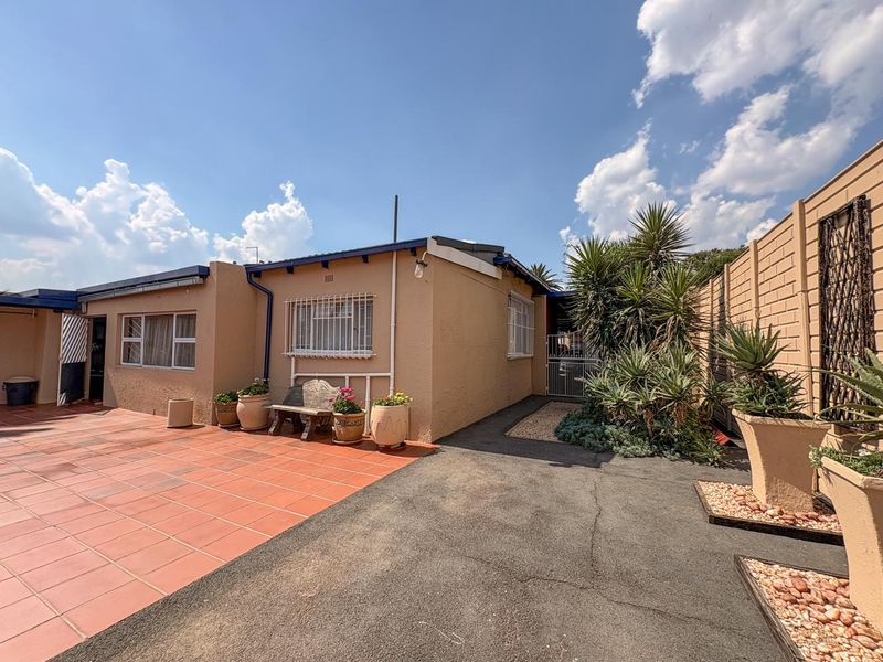 Rear exterior view of the property featuring a tiled patio area, paved driveway, and established garden beds with perimeter walling.