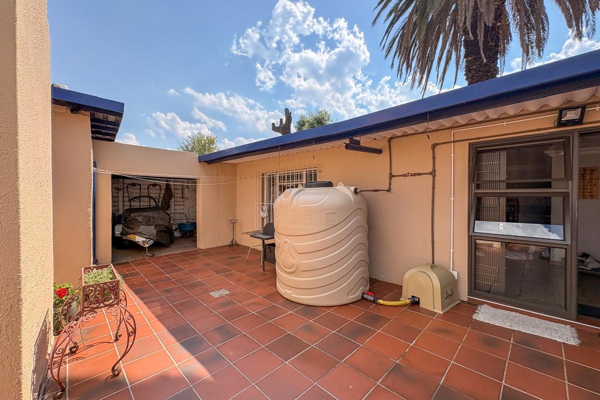 A paved rear courtyard area featuring a large water storage tank, external plumbing, and access to a covered storage or utility space.