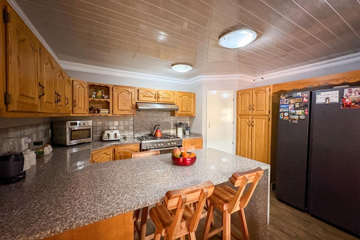 A functional kitchen featuring wooden cabinetry, granite-look countertops, a built-in stove with extractor fan, and a breakfast bar island.