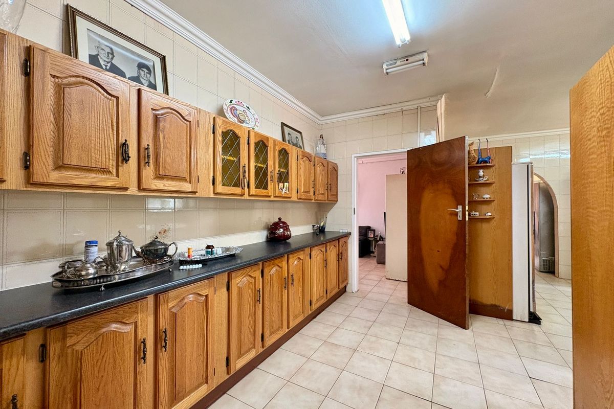 A dated kitchen featuring traditional oak-style cabinetry, dark laminate countertops, and ceramic floor tiling, offering a functional layout with potential for modernization.