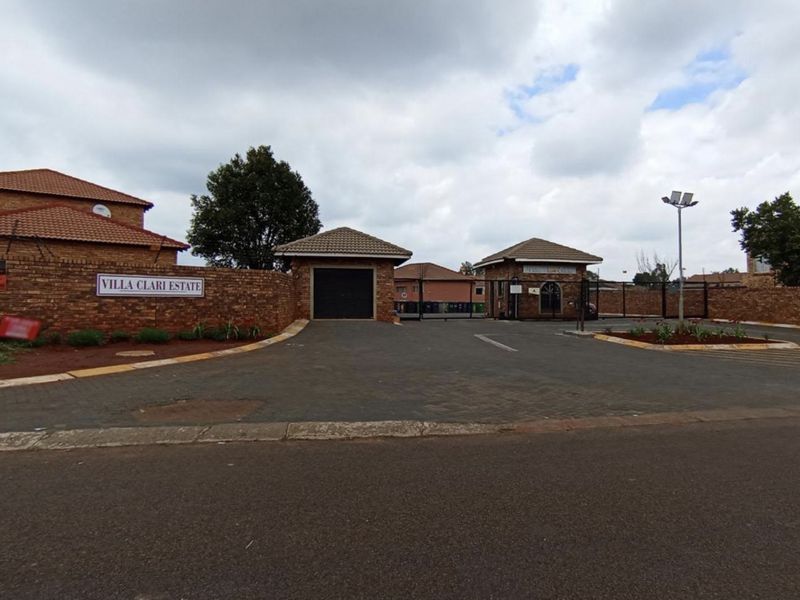 The entrance to Villa Clari Estate, featuring a brick perimeter wall, secure gated access, and paved driveway.