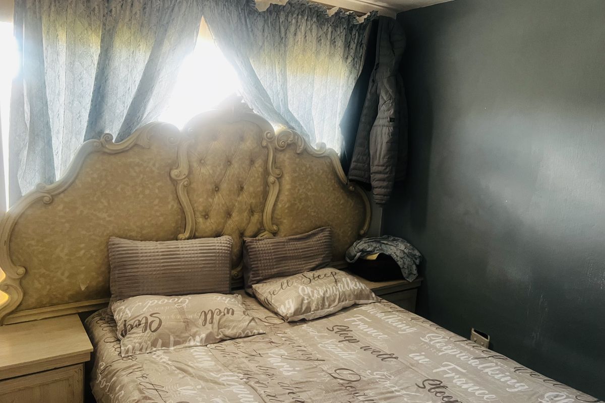 A bedroom featuring a large ornate headboard, neutral wall tones, and natural light filtering through window curtains.