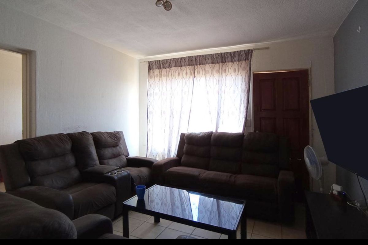 A living room featuring tiled flooring, a wooden door, and a large window with curtains, providing a functional and comfortable living space.