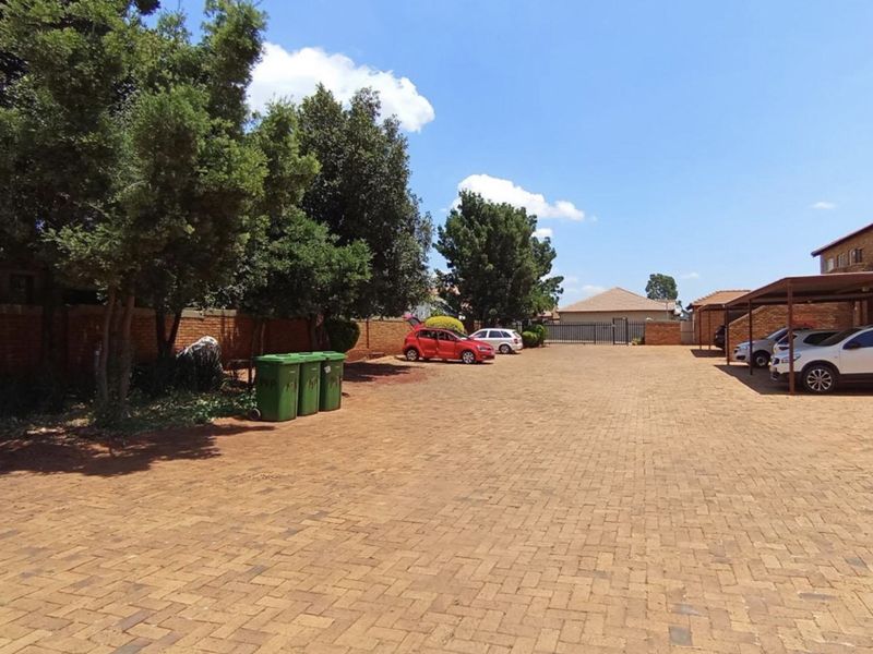 A paved parking area with covered carports and brick boundary walls, providing convenient off-street parking for the apartment complex.