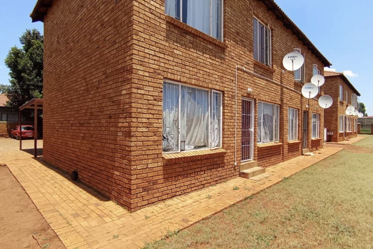 Exterior view of a multi-story brick apartment building featuring security bars on windows and multiple satellite dishes mounted on the facade.