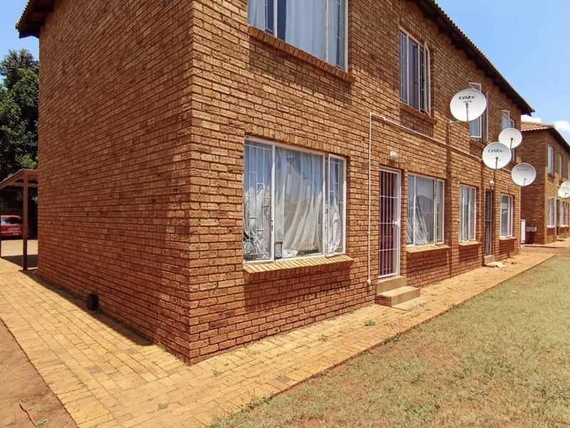 Exterior view of a multi-story brick apartment building featuring security bars on windows and multiple satellite dishes mounted on the facade.