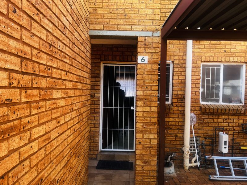 The entrance to unit 6 features a face-brick facade, a secure metal security gate, and a paved exterior area with integrated plumbing fixtures.